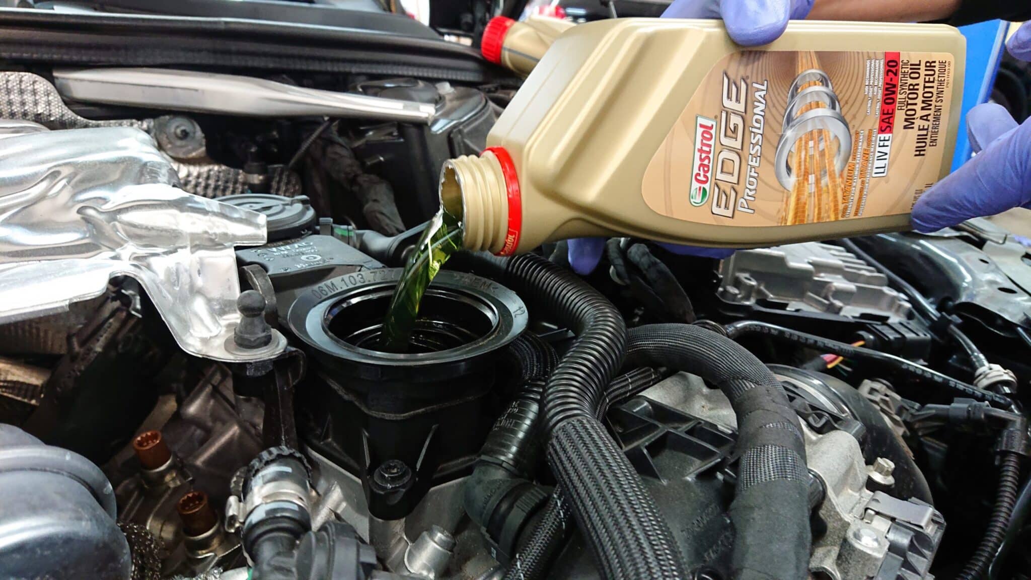 Blue-gloved hands pour Castrol EDGE Professional motor oil into a car's engine oil filler