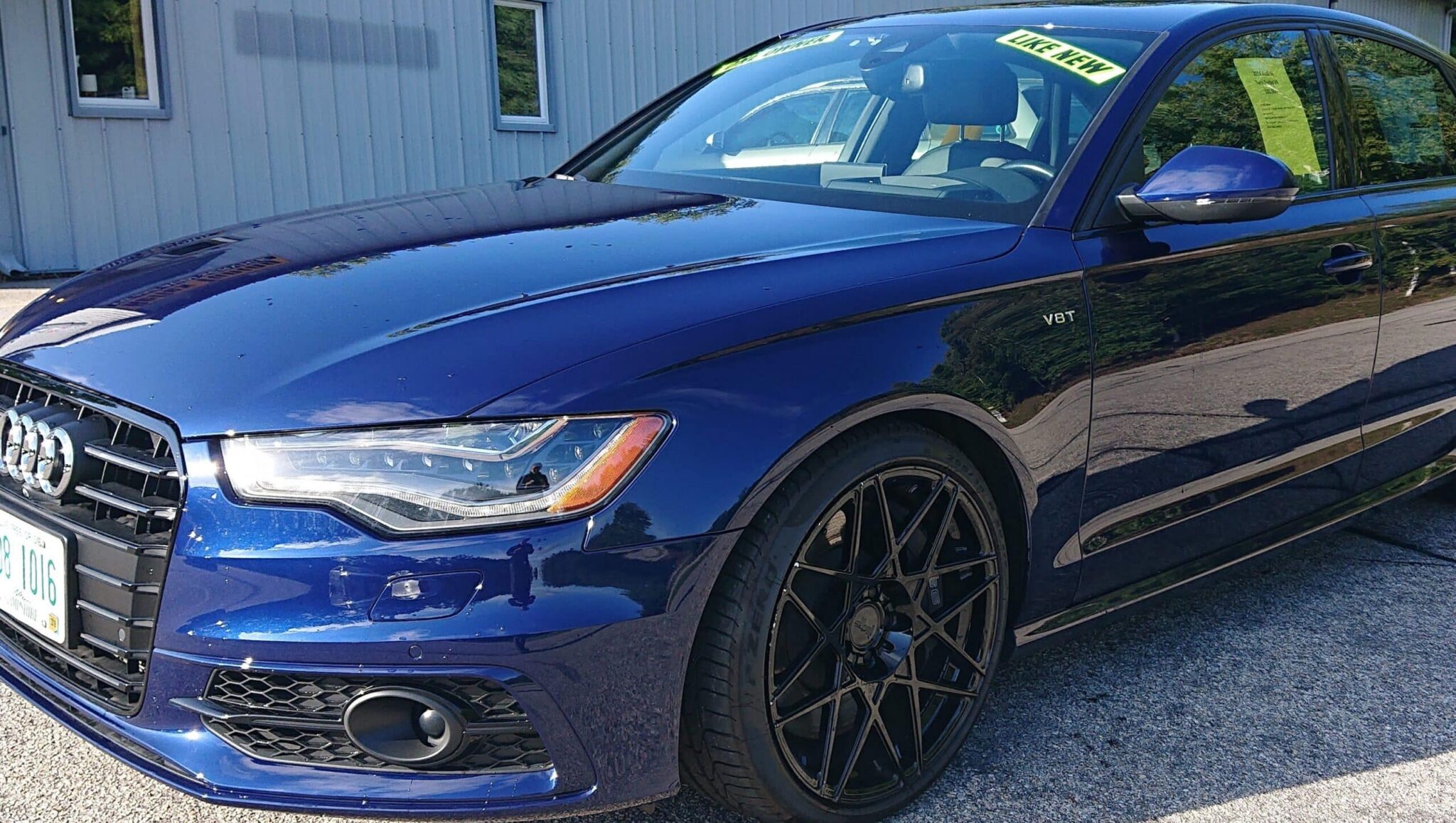 Blue Audi sedan with V8T badge, black wheels, and a 'LIKE NEW' sign on the windshield