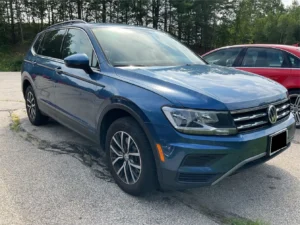 Audi VW Service A blue Volkswagen SUV is parked in a lot next to a red car, with trees in the background on a sunny day. Reflex Tuning, Hookett NH