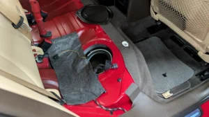 Audi VW Service A car’s back seat is removed, exposing the red metal floor and the fuel pump access panel. Various wires and a loose piece of fabric are visible near the opening, with carpet and seat parts pushed aside. Reflex Tuning, Hookett NH