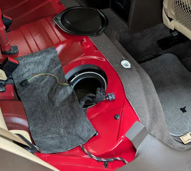 Audi VW Service A car’s back seat is removed, exposing the red metal floor and the fuel pump access panel. Various wires and a loose piece of fabric are visible near the opening, with carpet and seat parts pushed aside. Reflex Tuning, Hookett NH