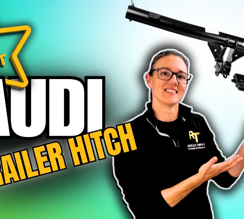 Audi VW Service A person wearing glasses and a black shirt gestures toward a car trailer hitch, with bold text reading The Best Audi Trailer Hitch against a gradient background. Reflex Tuning, Hookett NH