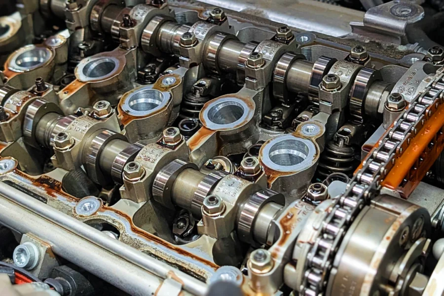 Audi VW Service Close-up view of a car engine’s valvetrain, showing camshafts, valve springs, gears, and timing chain with visible metal components and oily surfaces. Reflex Tuning, Hookett NH