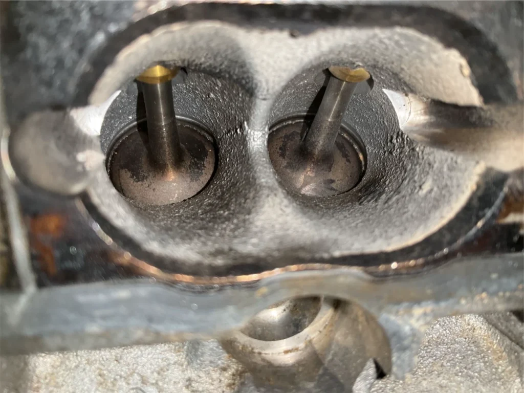 Audi VW Service Close-up view of two intake valves inside an engine cylinder head, showing carbon buildup and some metal surfaces with signs of wear and use. Reflex Tuning, Hookett NH