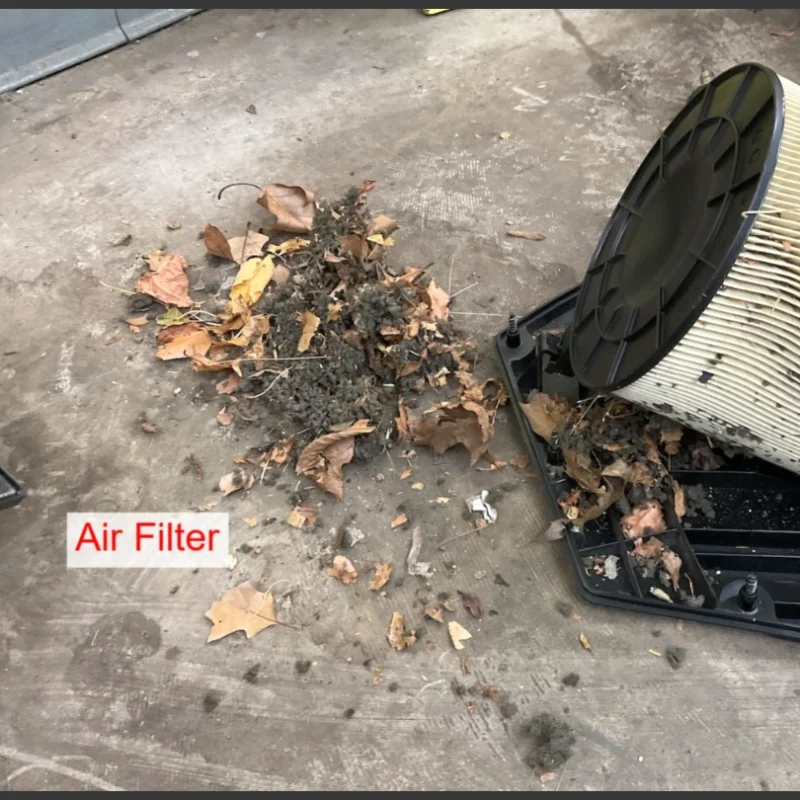 Audi VW Service A dirty air filter removed from its casing sits beside a pile of dust, dirt, and dry leaves on a concrete floor. The label Air Filter is visible near the filter. Reflex Tuning, Hookett NH