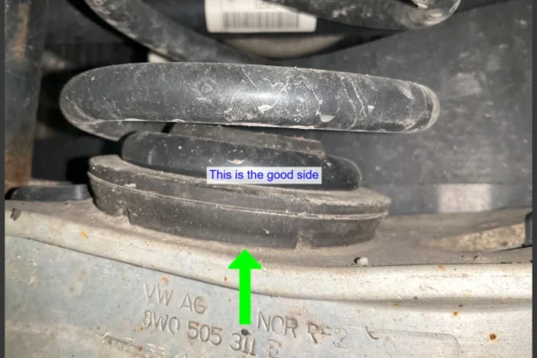 Audi VW Service Close-up of a car suspension coil spring and rubber mount, with a green arrow pointing up and a label that reads This is the good side placed above the rubber mount. Car part numbers are visible on the metal below. Reflex Tuning, Hookett NH