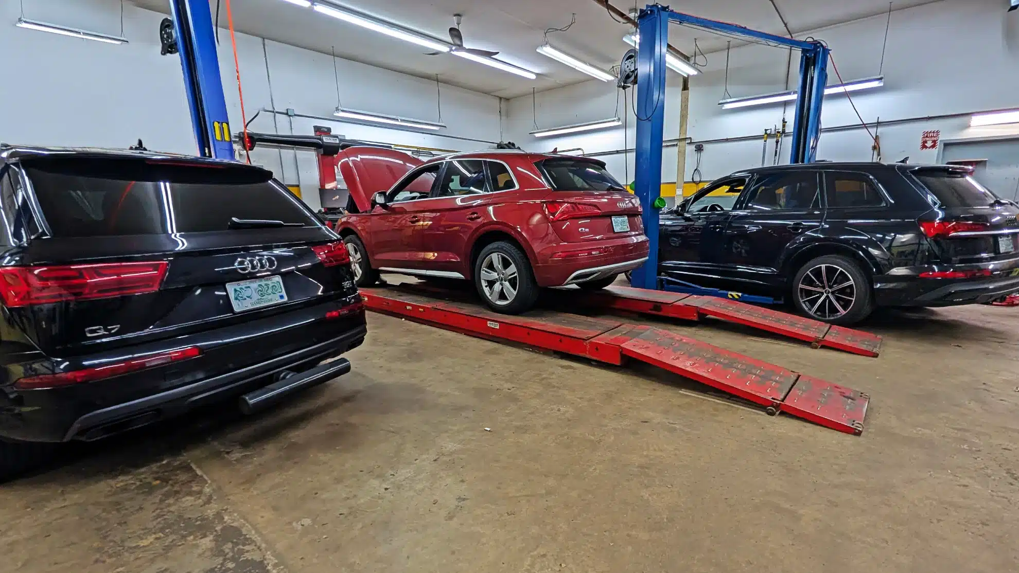 Three SUVs in Reflex Tuning, an Audi/Volkswagen shop in Hooksett, NH; red one on lift, hood open.