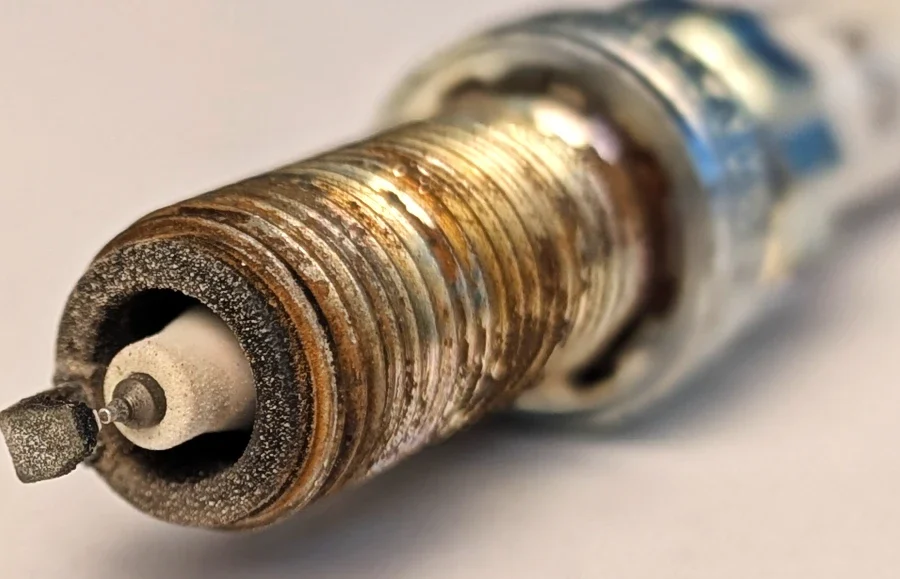 Audi VW Service A close-up of a used and dirty spark plug, showing rust, corrosion, and grime on its metal threads and electrode. Reflex Tuning, Hookett NH