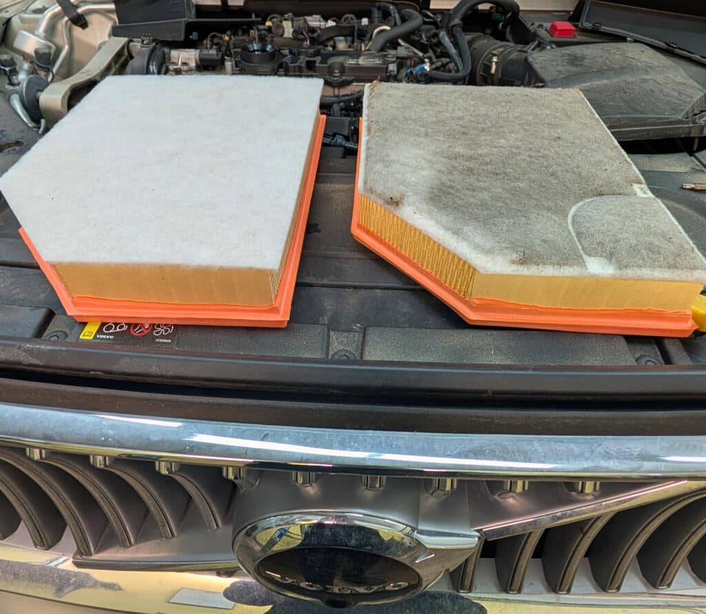 Two air filters, one clean and one dirty, are placed on the engine cover of a vehicle at Reflex Tuning in Hooksett, NH.